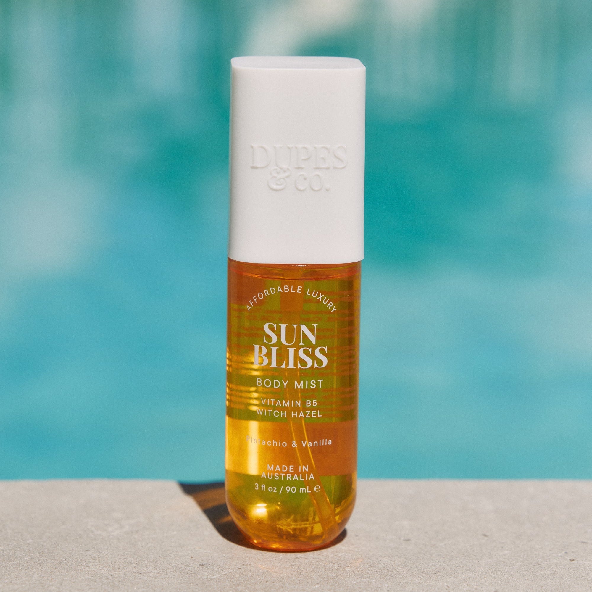 A bottle of Sun Bliss body mist with pistachio and vanilla scents, positioned near a poolside.
