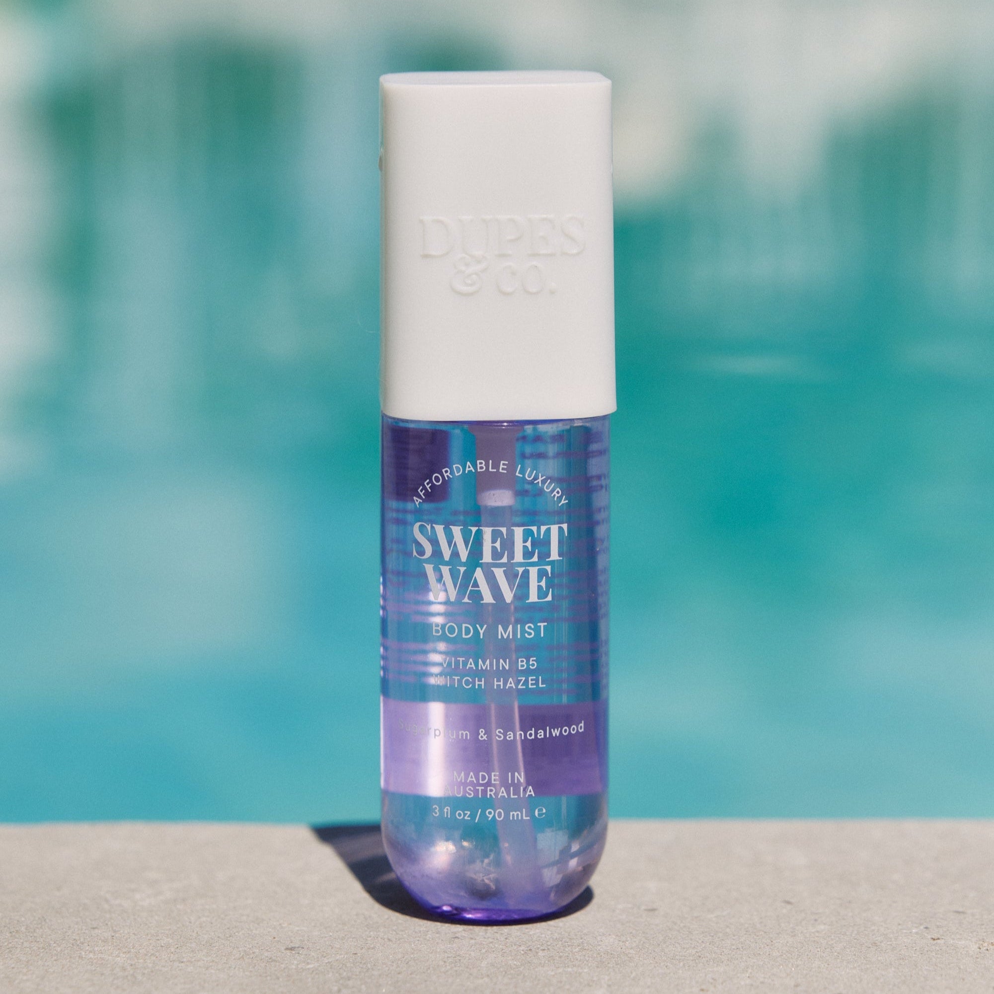 A bottle of Sweet Wave body mist with plum and vanilla orchid, placed near a poolside.
