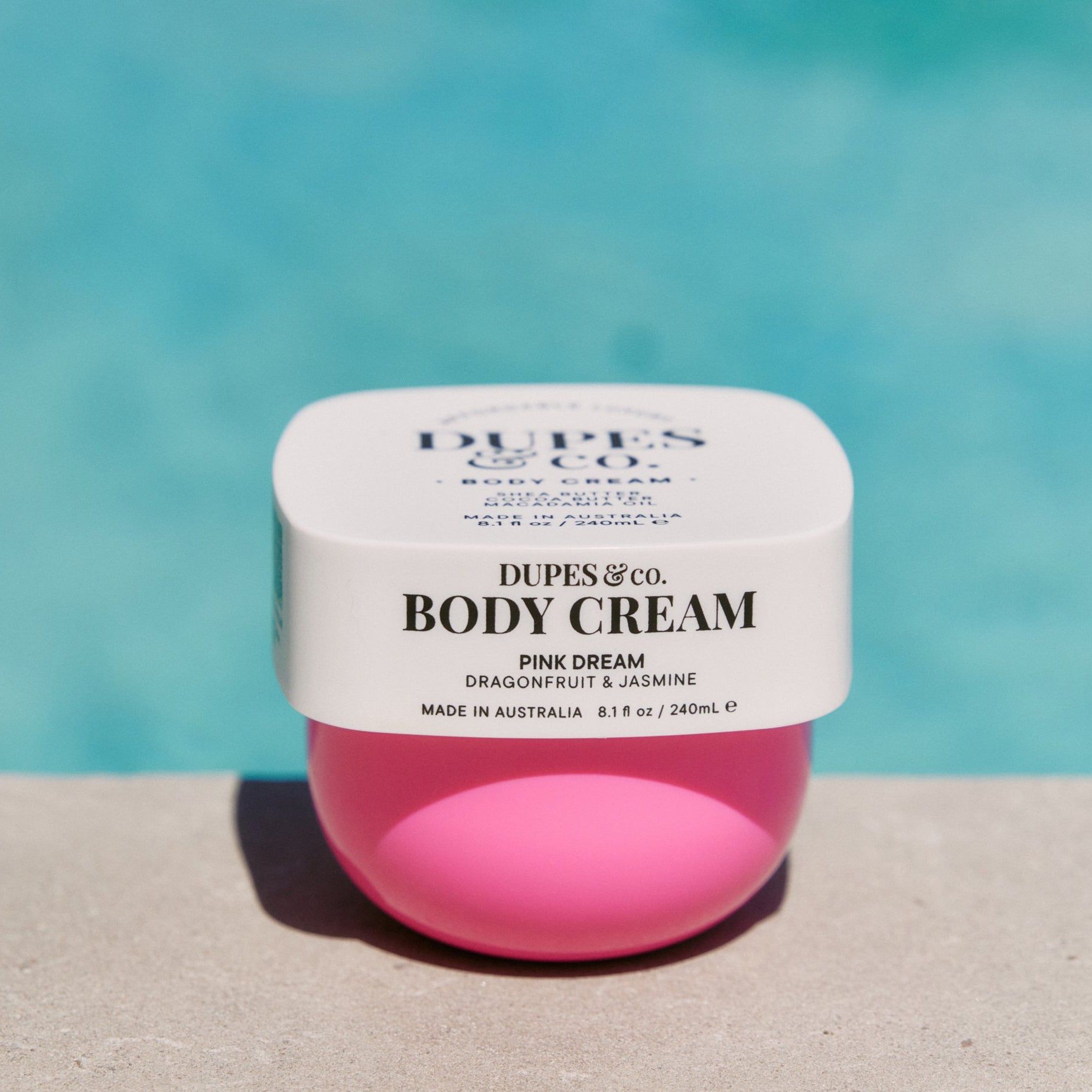 Pink body cream jar with white label against a blue background