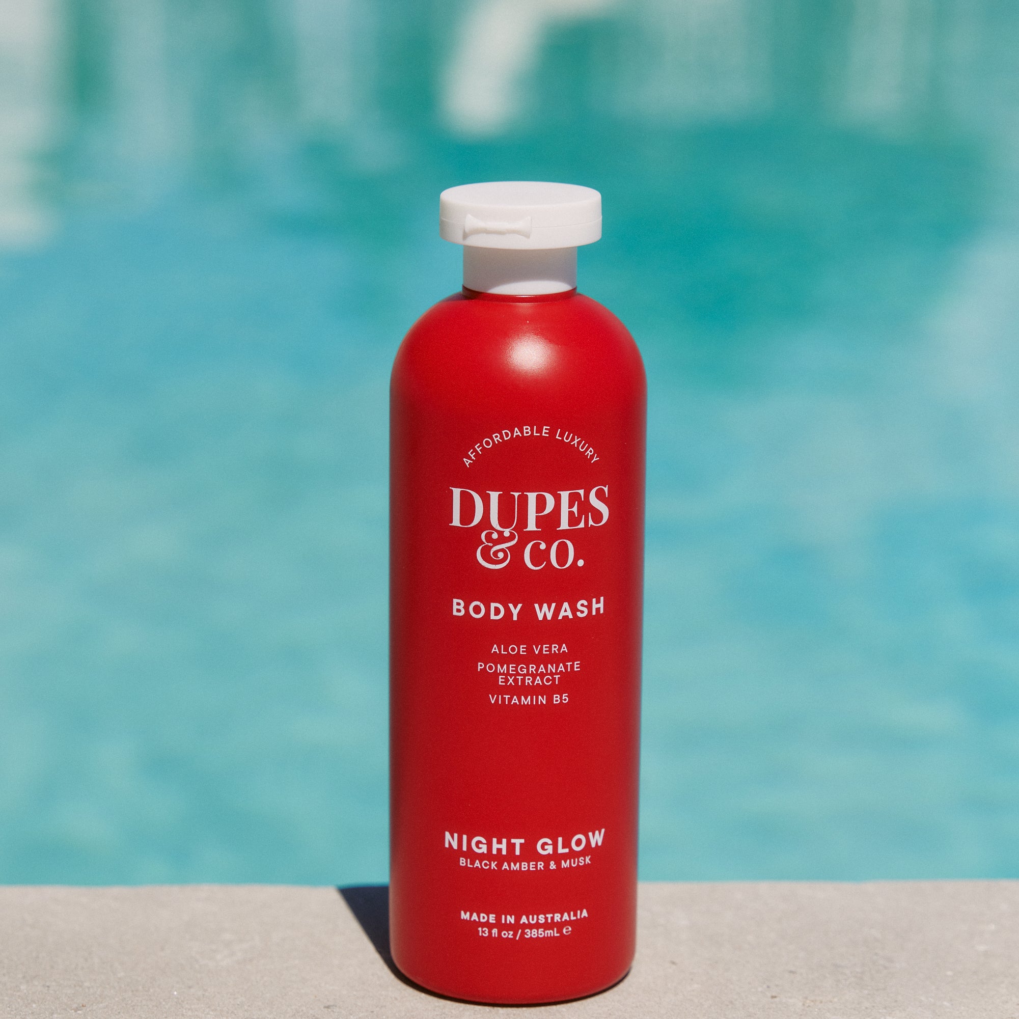 Red bottle of Dupes & Co. body wash with a pool in the background